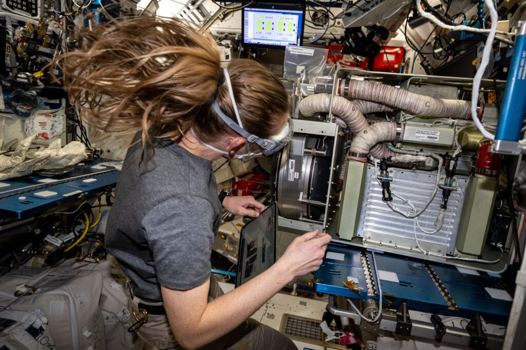 Woman works on device with air hoses in space station.